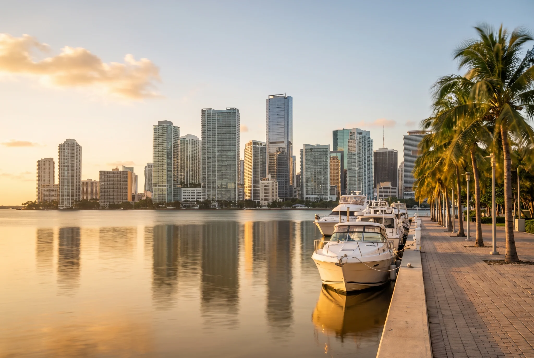 The Brickell skyline reflected in Biscayne Bay at golden hour, with boats and palm trees on the waterfront