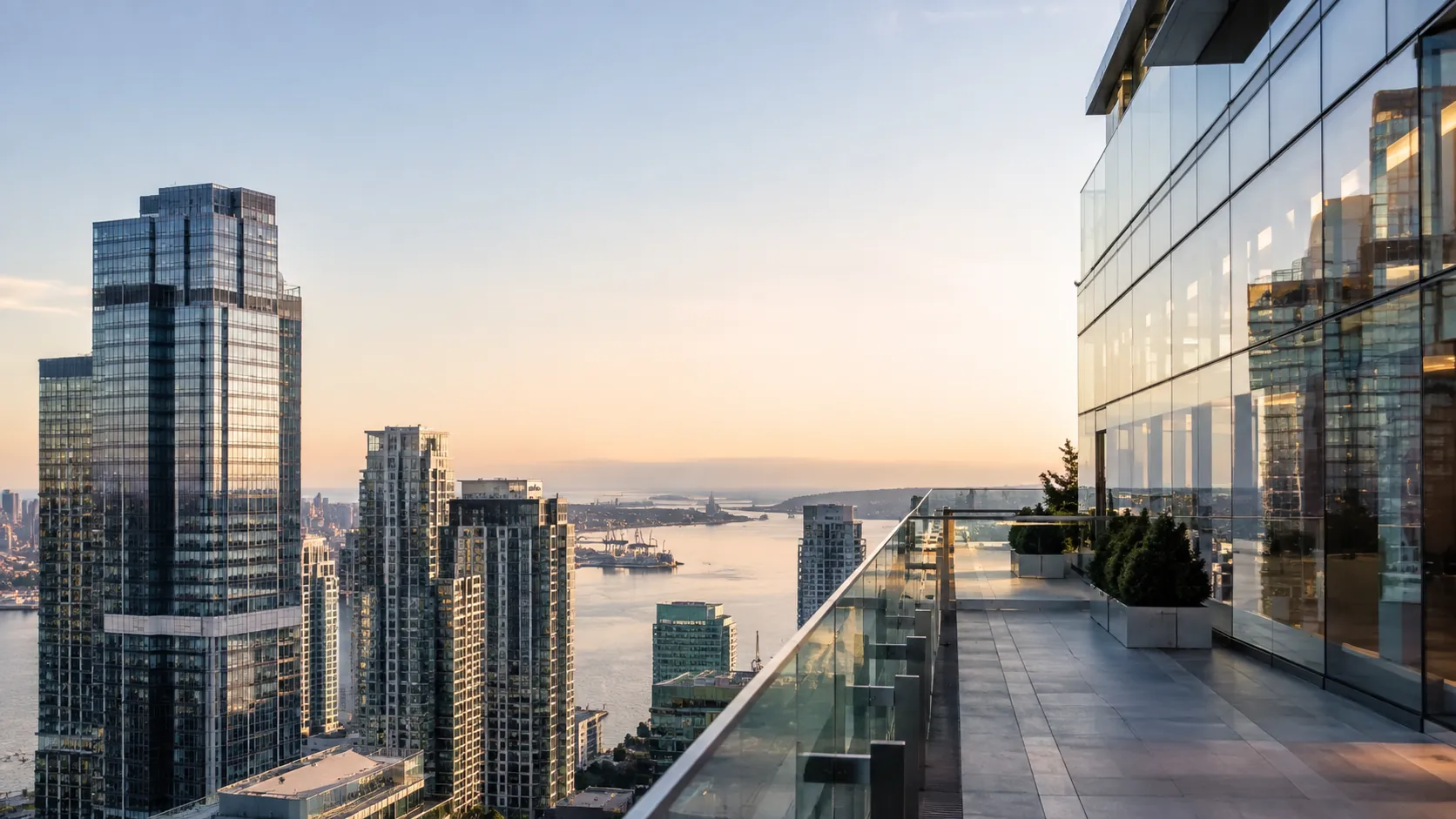 Terrace with glass railing overlooking Manhattan towers and the harbor at sunset